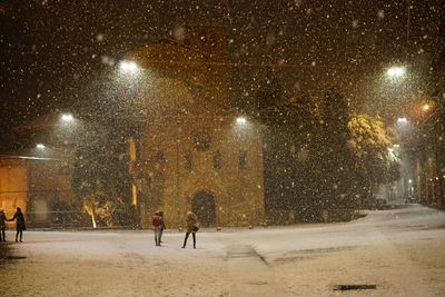 People walking on snow covered street at night