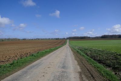 Road passing through agricultural field against sky