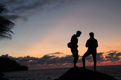 Silhouette men standing on beach against sky during sunset