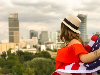 Side view of mid adult woman with american flag in city standing against cloudy sky