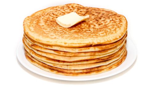 Close-up of pancakes with butter in plate on white background