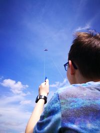 Low angle view of boy flying kite against blue sky during sunny day