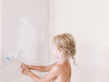 Shirtless girl painting door by wall at home