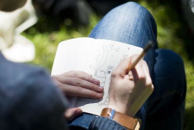 Midsection of person drawing in book at park