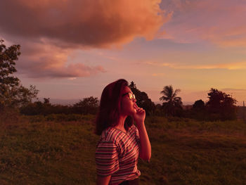 Woman standing on field against sky during sunset