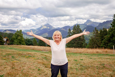 Emotional elderly woman stands among mountains with outstretched arms. active aging, inner peace