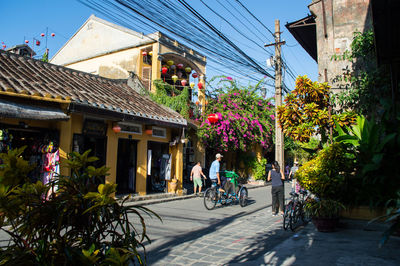 People riding bicycle on street amidst houses against sky