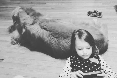 High angle view of girl using phone while leaning on dog at home