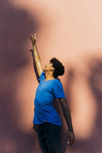 Young man with hand raised standing in front of wall