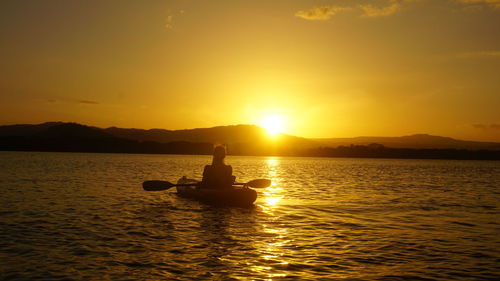 Silhouette man on boat in sea against sky during sunset