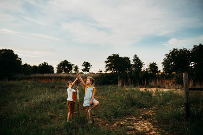 Brother and sister standing in open field at sunset