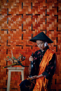 Young woman wearing hat standing against orange wall