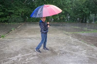 Portrait of boy standing with umbrella on road during rain