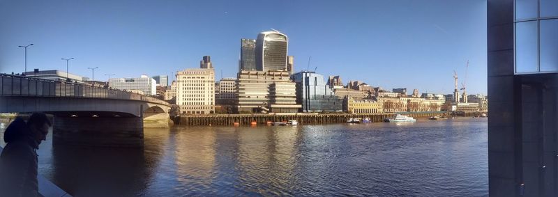 Bridge over river by buildings against clear blue sky