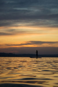 Silhouette men in sea against sky during sunset