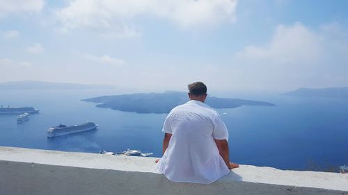 Rear view of man sitting on retaining wall against sea