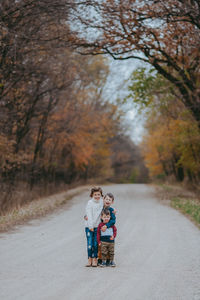 Girl standing with brothers on road during autumn