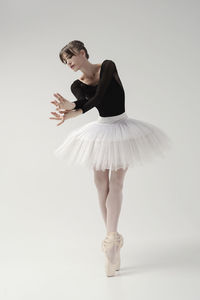 A ballerina in a bodysuit and tutu poses in motion showing ballet elements while standing on pointes