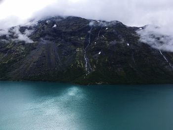 Scenic view of sea by mountain against sky