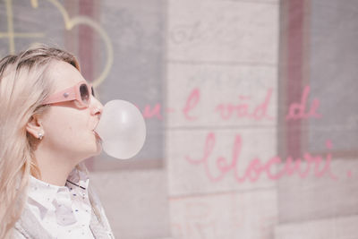 Side view of woman blowing bubble gum by glass window