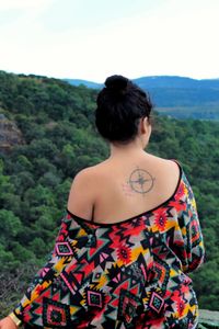 Rear view of young woman with tattoo on back sitting against sky