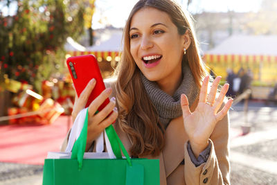 Girl say hello in video calling with telephone carrying shopping bags on christmas time outdoors