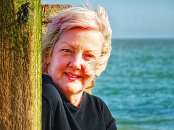 Close-up portrait of mature woman by wooden post at beach