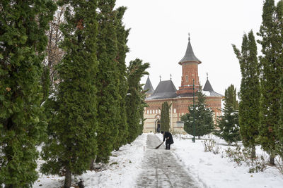 Woman walking by building against clear sky during winter