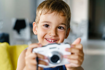 Portrait of boy holding camera while sitting at home