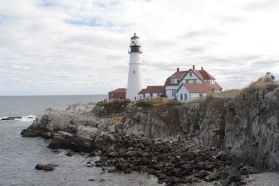 Lighthouse by sea and buildings against sky