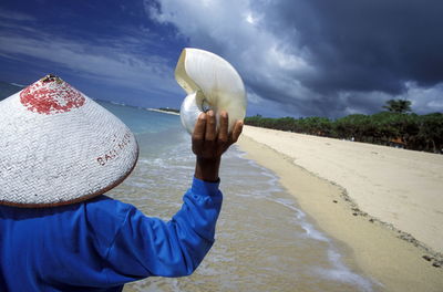 Rear view of man holding seashell at beach