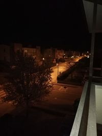 Illuminated street by buildings in city at night