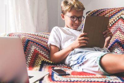 Boy using mobile phone while sitting on bed at home