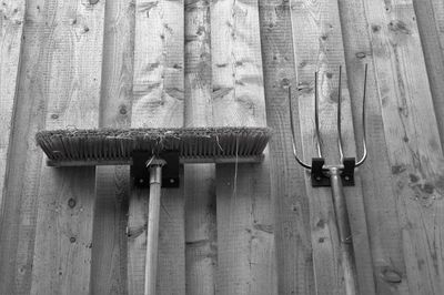 Low angle view of broom and gardening fork against wooden wall