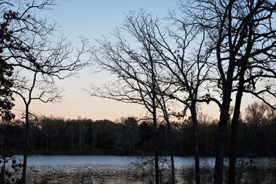 Silhouette bare trees by lake against sky during sunset