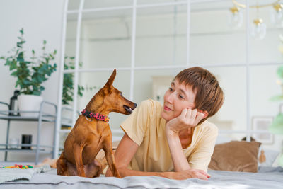 Mature woman lies on floor with small miniature pinscher, enjoying