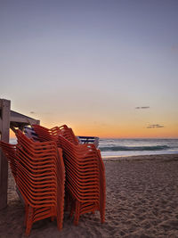 Hooded chairs on beach against sky during sunset