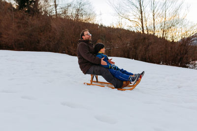 Father and daughter together on wooden sled going down the snowy hill