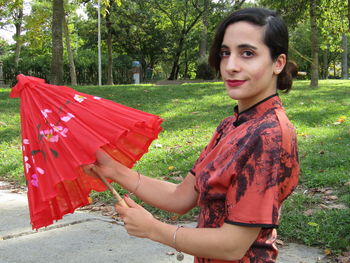 Portrait of smiling young woman holding red while standing outdoors