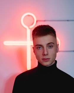 Portrait of young man standing illuminated neon light on wall