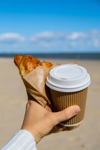 Cropped hand of woman holding coffee at beach