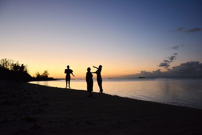 Silhouette people standing on beach against sky during sunset