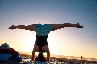 Rear view of woman doing handstand at beach against clear sky