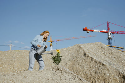 Smiling woman watering plant at construction site