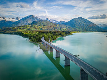 Road leading towards mountains by lake against sky