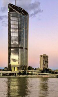 Modern building by river against sky during sunset