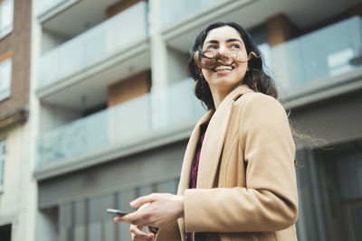 Happy woman with mobile phone in front of building