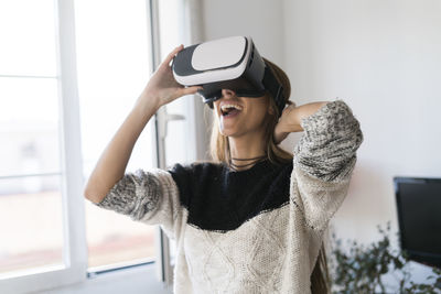 Excited young woman wearing vr glasses at home