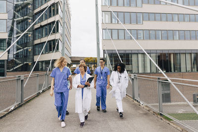 Multiracial healthcare workers discussing while walking on bridge by hospital building