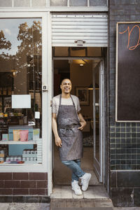 Happy male deli owner wearing apron leaning on doorway